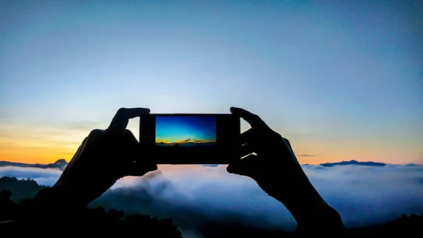 Mano sosteniendo el teléfono disparando el sol de la mañana y la niebla. — Foto de Stock