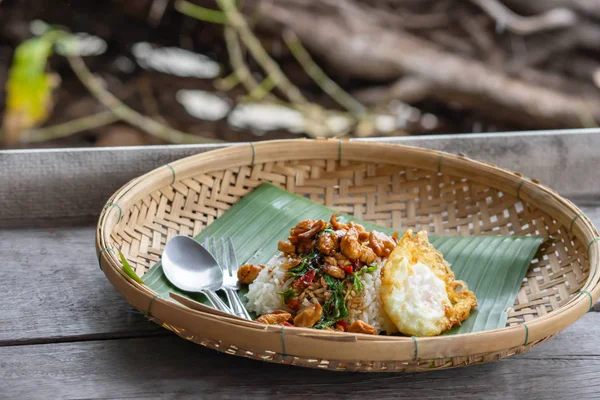 Mexa a folha de manjericão frito Frango com arroz e coloque o ovo frito na cesta de bambu na mesa de madeira . — Fotografia de Stock