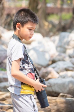 Elinde kamera tutan Asyalı çocuk. Tayland 'ın Chumphon kentindeki Laem Kho Kwang Sahili' nde kayalar ve ağaç var. 18 Mart 2020