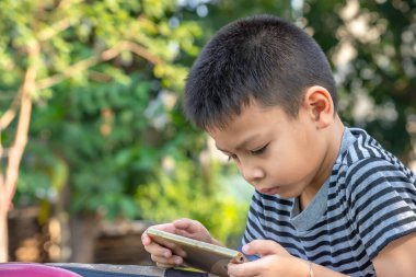 Asyalı çocukların portresi parkta cep telefonu çalıyor.