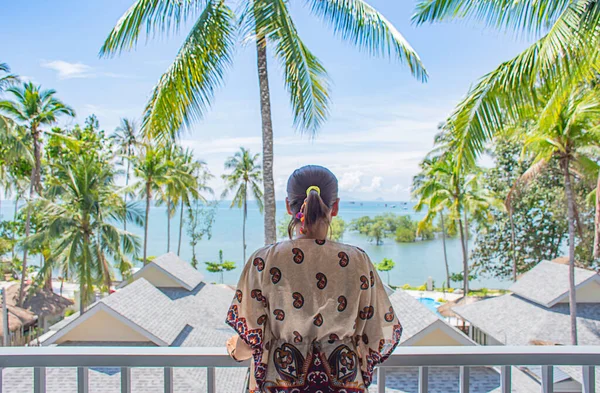 The image behind the women looked at the sea and coconut trees  on the balcony.