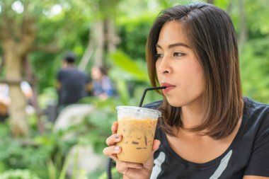 Asyalı kadın elinde bir bardak soğuk espresso kahve tutuyor. Arka plan bulanık görünüyor..