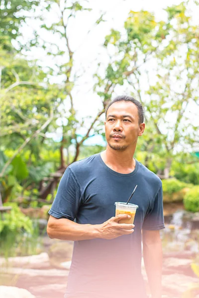 Asian man holding a glass of cold espresso coffee Background blurry views tree.