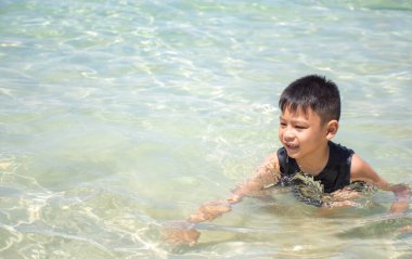 Siyah tişörtlü Asyalı bir çocuğun portresi denizde oturuyordu..