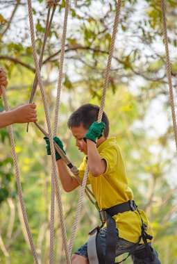 Asean çocuk halatı sallıyor ve mutlu bir şekilde gülümsüyor. Arka plan bulanık ağacı..