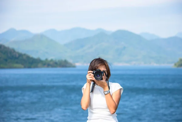 Hand woman holding the camera Taking pictures background Kaeng Krachan dam phetchaburi , Thailand.