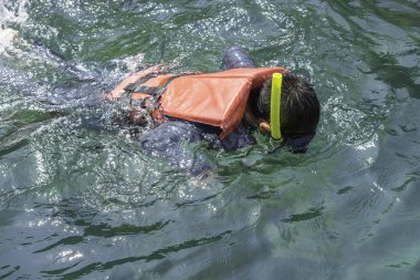 Asyalı çocuk can yeleği giyiyor ve dalgıçlık yapıyor..