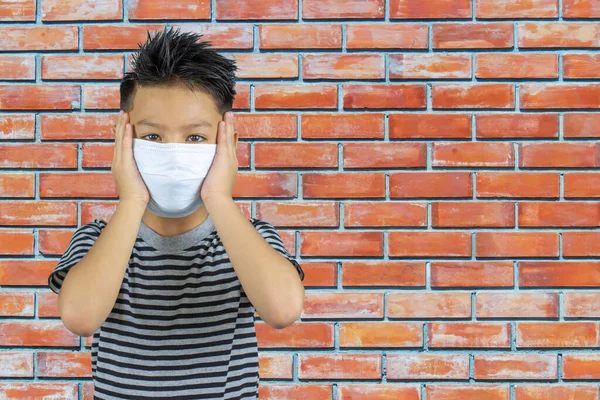 アジアの少年の顔にマスクを保持手レンガの壁 — ストック写真