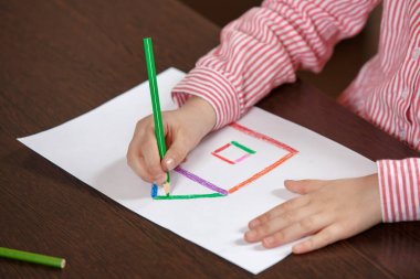 Evde kapalı renkli kalemlerle renkli bir ev çizen çocuk ellerini kapatın.