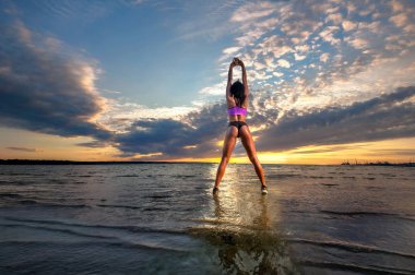 Gün batımında sahilde deniz Körfezi'nin suda egzersiz genç atletik kadın 