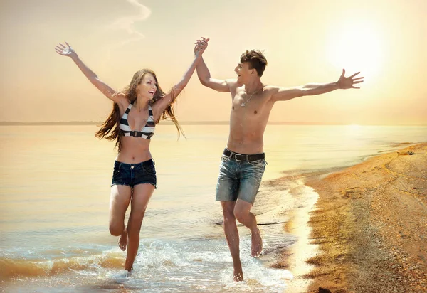 年轻快乐欢快的夫妇一起运行在海滩上日落 — 图库照片