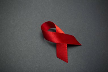 Koyu gri arka planda kırmızı kurdele. Dünya AIDS Günü 'nün ya da kanserin ya da HIV Farkındalık Ayı' nın ve sağlık hizmetleri kavramının sembolü. Boşluğu kopyala.
