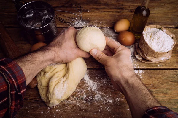 Ev mutfağında pizza hamuru pişiyor. Ekmek, pizza, börek ve ekmek için ev yapımı hamur işi. Ahşap bir arka planda hamur malzemeleri (un, yumurta, tereyağı).