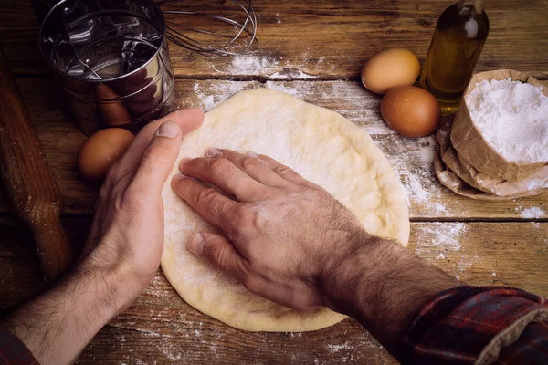 Ev mutfağında pizza hamuru pişiyor. Ekmek, pizza, börek ve ekmek için ev yapımı hamur işi. Ahşap bir arka planda hamur malzemeleri (un, yumurta, tereyağı).