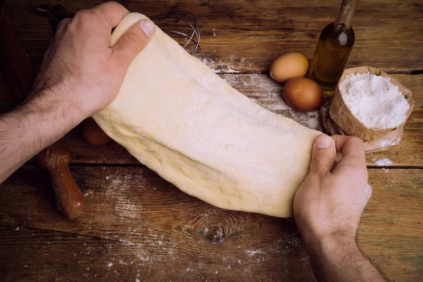 Ev mutfağında pizza hamuru pişiyor. Ekmek, pizza, börek ve ekmek için ev yapımı hamur işi. Ahşap bir arka planda hamur malzemeleri (un, yumurta, tereyağı).