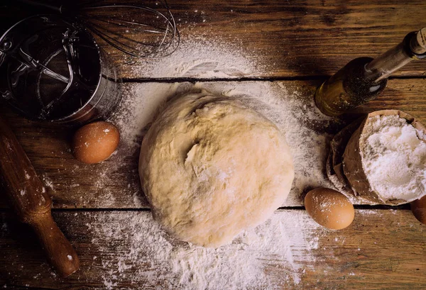 Ev mutfağında pizza hamuru pişiyor. Ekmek, pizza, börek ve ekmek için ev yapımı hamur işi. Ahşap bir arka planda hamur malzemeleri (un, yumurta, tereyağı).