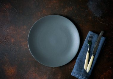 Karanlık bir arka planda boş bir plaka. Yemek için çatal ve bıçakla dolu boş gri seramik tabak ve güzel bir arka planda akşam yemeği..
