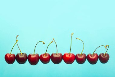 Kiraz arkaplanı çok az. Mavi arkaplanda kırmızı yaz kiraz üzümleri. Yaz meyveleri ve gıda konsepti.