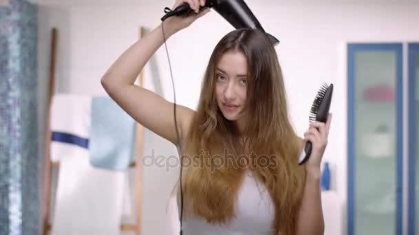 Young attractive woman blow-dries and brushes her long brown hair — Stock Video