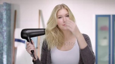 Genç sarışın bir kadın blow-dries ve bir ayna önünde saç fırçaları