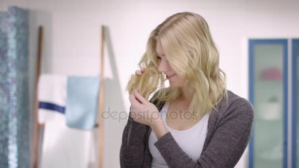 Блондинка приваблива жінка дивиться на волосся з посмішкою на її обличчі — стокове відео