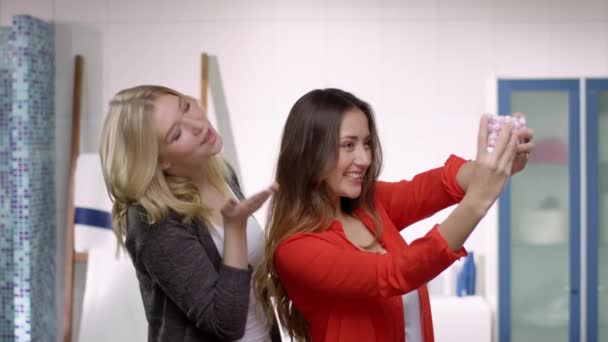 Twee jonge mooie vrouw doen poses en nemen van foto's met een mobiele telefoon in een moderne badkamer met een heleboel plezier — Stockvideo