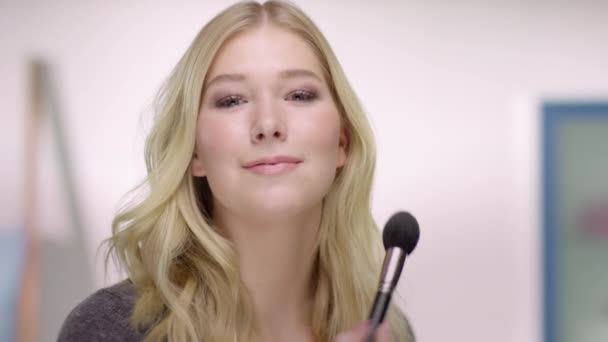 Joven mujer rubia atractiva está aplicando maquillaje en su mejilla — Vídeos de Stock