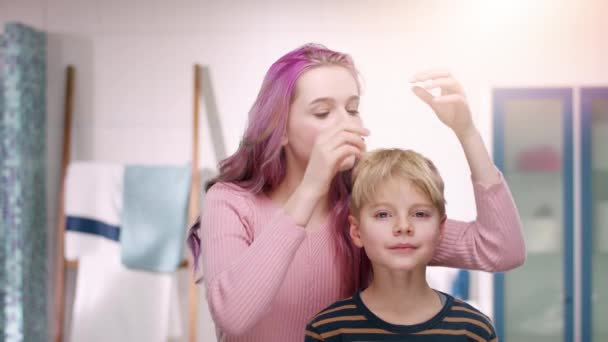 Giovane ragazza è styling i capelli del suo fratellino davanti alla fotocamera — Video Stock