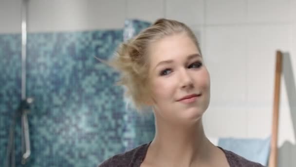 Jonge blonde vrouw blow-dries en haar haar voor een spiegel borstels — Stockvideo