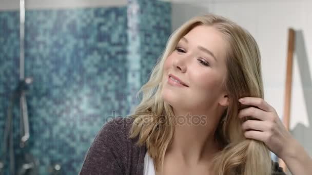 Mulher loira está escovando o cabelo na frente de um espelho — Vídeo de Stock