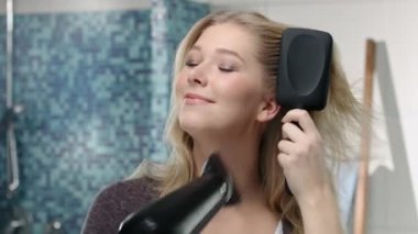 Genç sarışın bir kadın blow-dries ve banyoda saç fırçaları