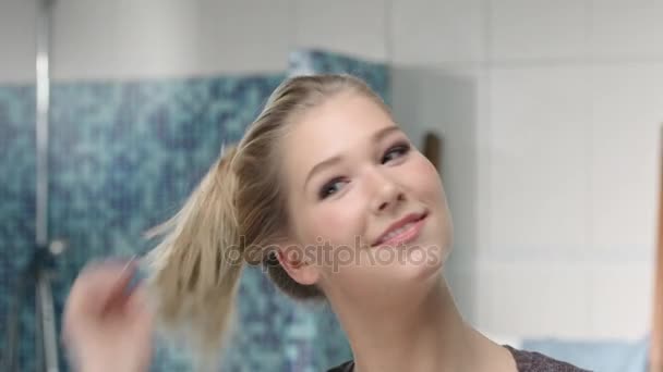 Aantrekkelijke blonde vrouw opent haar vlecht met een wishful glimlach voor een spiegel — Stockvideo