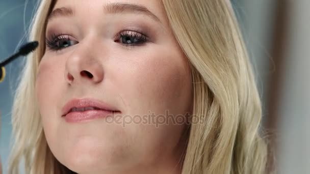 Mujer caucásica joven está aplicando rímel en sus pestañas — Vídeos de Stock