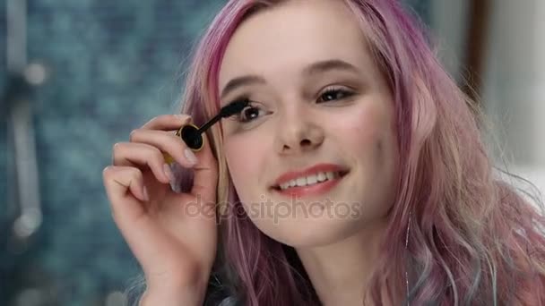 Jeune femme à la puberté avec les cheveux roses essaie mascara à ses cils — Video