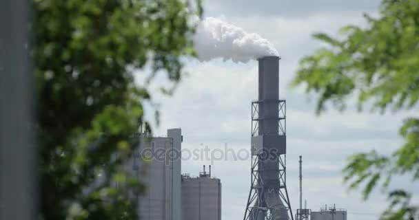 Вид на промисловий завод з димоходом і зеленими деревами на передньому плані — стокове відео