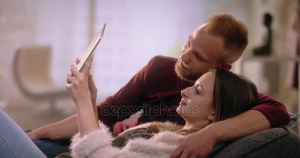 Pareja joven enamorada en el sofá de casa usando una tableta — Vídeos de Stock