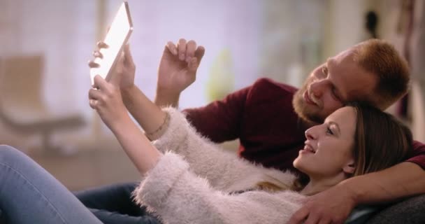 Νέοι oouple με αγάπη στον καναπέ σπίτι κάνοντας μια selfie με tablet — Αρχείο Βίντεο