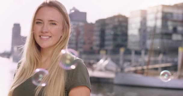 Приваблива блондинка посміхається в камеру з вибуховими бульбашками, що літають — стокове відео