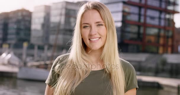 Attraente donna bionda sorridente nella fotocamera davanti alla città moderna — Video Stock