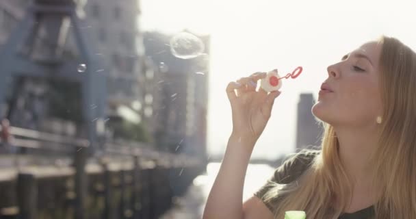 Mulher loira atraente fazendo bolhas estourando infronto de um porto moderno — Vídeo de Stock