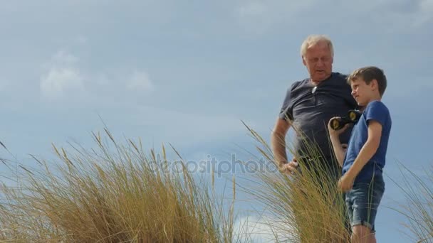 Дедушка что-то говорит своему внуку в бинокль — стоковое видео