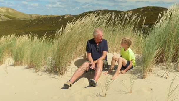 爷爷和孙子坐在沙滩上和对方说话 — 图库视频影像