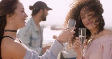 İki genç kadın arka arkaya, gözlük ellerinde ve arkadaşları arka planda dans