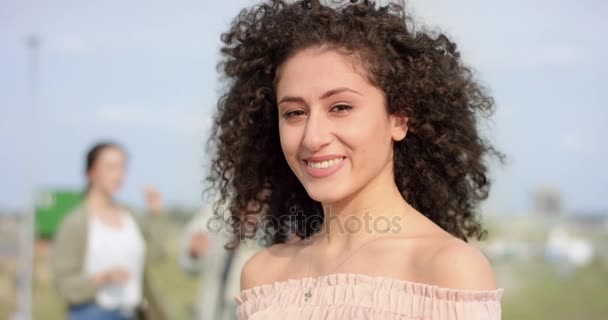 Mladá žena s tmavými vlasy zkroucený úsměv do kamery s přáteli v pozadí — Stock video