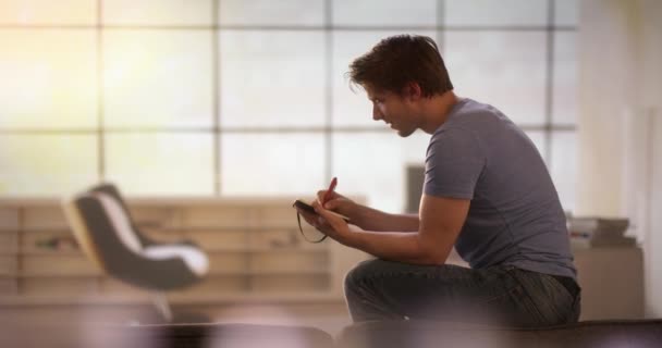 Junger Mann macht sich Notizen, während er auf einer Couch sitzt — Stockvideo