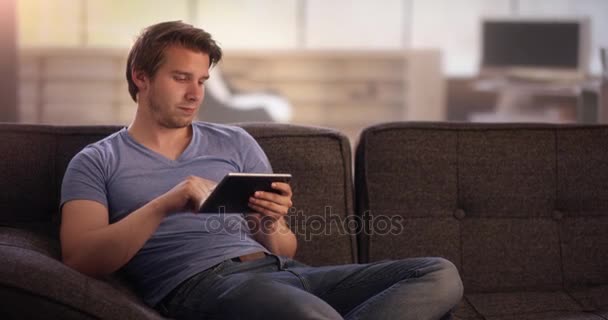 Молодой человек на диване с помощью планшета — стоковое видео