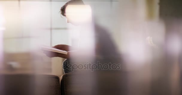 Νεαρός άνδρας, διαβάζοντας ένα βιβλίο σε έναν καναπέ — Αρχείο Βίντεο