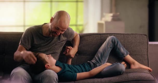 Vater kitzelt seinen Sohn auf der Couch — Stockvideo