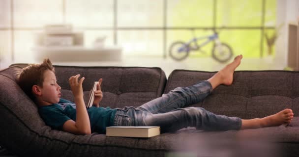 Boy změny smartphone proti knize na gauči — Stock video