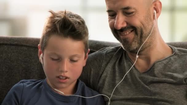 Padre e hijo con auriculares en el sofá — Vídeos de Stock